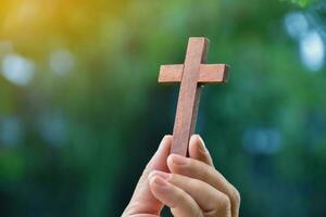 Wooden cross holding in hand with green and fresh forest background, concept for love of god in people around the world. photo