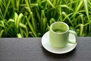 A cup of green tea on wooden table beside flower bed. photo