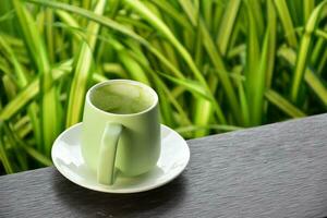 A cup of green tea on wooden table beside flower bed. photo