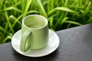 A cup of green tea on wooden table beside flower bed. photo