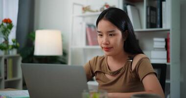 imágenes de contento joven asiático mujer trabajando con ordenador portátil en un escritorio en el vivo habitación a hogar. estilo de vida, actividad y personas conceptos. video