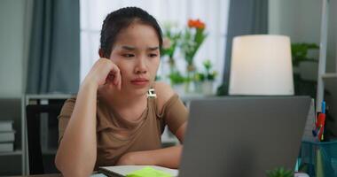 métrage de ennuyé Jeune asiatique femme travail avec portable sur une bureau dans le vivant pièce à maison. mode de vie, activité et gens concepts. video