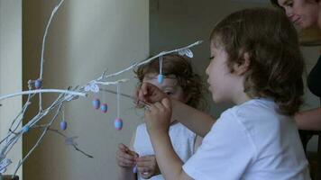 Brother and his smaller sister are hanging decorative Easter eggs on painted tree twigs. video