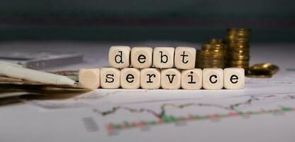 Words DEBT SERVICE composed of wooden letter. Stacks of coins in the background. photo