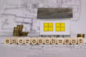 Word  ENCROACHMENT composed of wooden letters. Small paper house in the background. photo