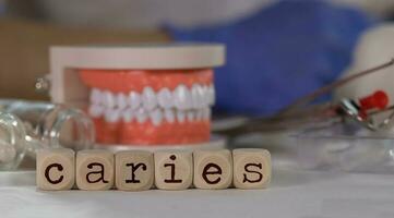 Word CARIES composed of wooden dices. Pills, documents, pen, human jaw model in the background. photo