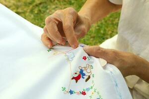 An old woman is embroidering on the white blanket photo