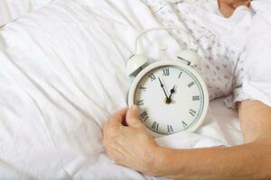 Vintage alarm clock on the bed of senior woman photo