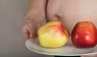 joven embarazada mujer mantiene un blanco plato con rojo manzanas en él. foto