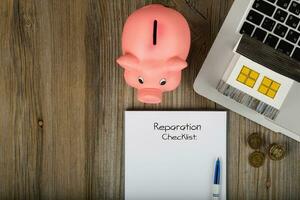 Reparation checklist is written on a sheet of paper. Pink piggy bank close to the laptop. photo