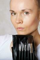 Young lady keeps make up brushes kit close to her face. Closeup photo