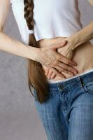 Young lady dressed in jeans has a pain in the belly. Closeup photo