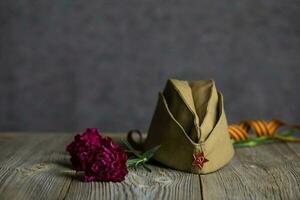 Military cap, carnations, Saint George ribbon on a wooden surface. photo