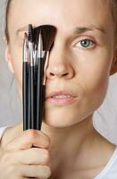 Young lady keeps make up brushes kit close to her face. Closeup photo