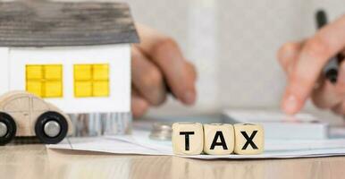 Word TAX composed of wooden letters. Female hand with a pen in the background. photo