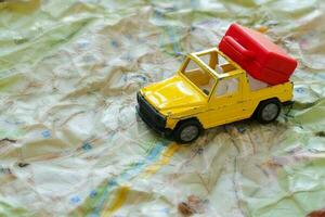 Mini car and a red plastic suitcase on a map. Closeup photo