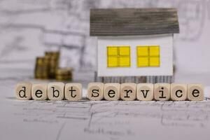 Word DEBT SERVICE composed of wooden letter. Small paper house in the background. photo