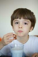 chico de seis años es tomando un vaso de calentar Leche con avena galletas. foto