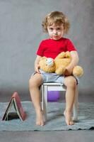 un chico de Tres años antiguo se sienta en un blanco silla. foto