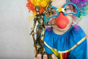 Statue of Themis in the hand of five years old child dressed in clown costume. photo