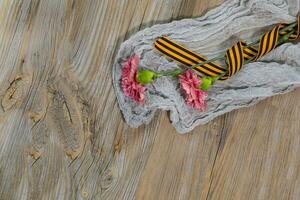 Two pink carnations, Saint George ribbon on a wooden surface. photo