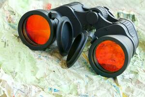 Black binoculars on a shrivelled map. Closeup photo