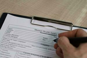 Female hand is filling up the mental health intake form and a pen on a table. photo