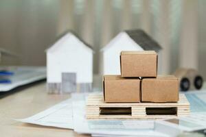 Pallet with carton boxes in front of small paper houses. photo