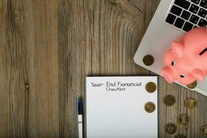 Year-End financial checklist. Pink piggy bank close to the laptop. photo