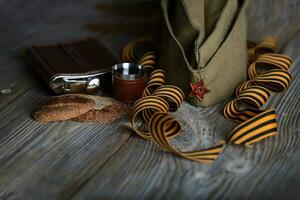 Military cap, carnations, Saint George ribbons, flask with alcohol  on a wooden surface. photo