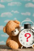 Question mark depicted on a vintage clock with academic cap. Brown plush teddy bear in the background. photo