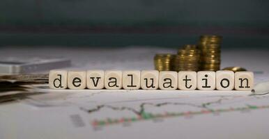 Word DEVALUATION composed of wooden letter. Stacks of coins in the background. photo