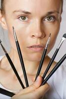 Young lady keeps make up brushes kit close to her face. Closeup photo