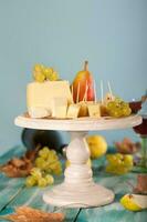 Cheese slices, pear, and grapes on a wooden stand. photo