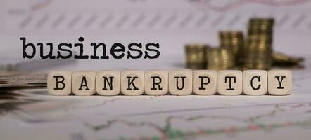 Words BUSINESS BANKRUPTCY composed of wooden letter. Stacks of coins in the background. photo