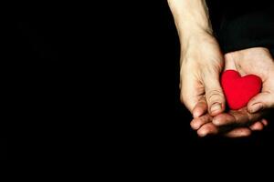 palma de un campesino mujer con felpa rojo corazón en un negro tela. foto