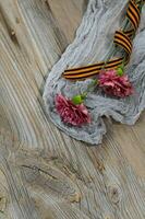 Two pink carnations, Saint George ribbon on a wooden surface. photo