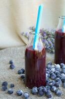 Glass bottle of blueberries juice on a sackcloth. Closeup photo