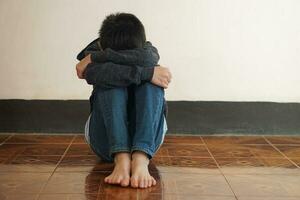 Deprimido chico se sienta solo en el piso, sensación triste y llorar, abrazo su rodilla. concepto , emocional expresión. culpable, negativo sentimiento. introvertido niño. ser acosado foto