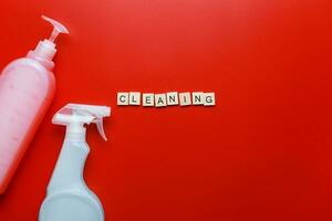 Flat lay cleaning products and sponges on a red background. Word cleaning from letters. Cleaning Spray Mockup photo