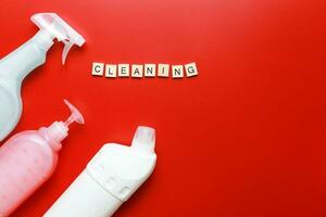 Flat lay cleaning products, cleaning spray on red background and sponges. Word cleaning from wooden letters photo