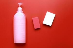 Flat lay dishwashing detergent and sponge on red background. Cleaning. photo