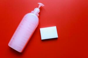 Flat lay dishwashing detergent and sponge on red background. Cleanliness cleaning photo