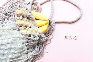 Flat lay bananas in a mesh bag. The word eco from wooden letters on a pink background. Zero waste photo