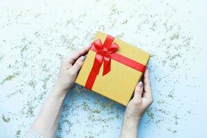 Hands holding a gift. Box with red bow. Sequins and glitter photo