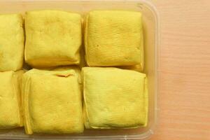 Tahu Kuning Cibuntu or Yellow tofu in the plastic container on the wooden background photo