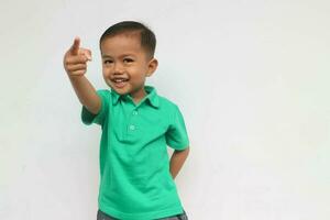 retrato de un contento pequeño asiático chico sonriente mientras señalando , aislado en el blanco antecedentes foto