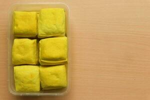 Tahu Kuning Cibuntu or Yellow tofu in the plastic container on the wooden background photo