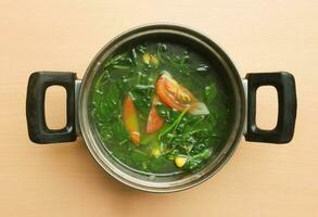 Sayur Bayam or Spinach clear soup serve in the pot isolated on wooden background photo