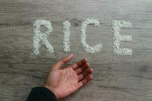 Open hand asking gesture, rice grains form the letter RICE on a wooden background. hunger concept photo